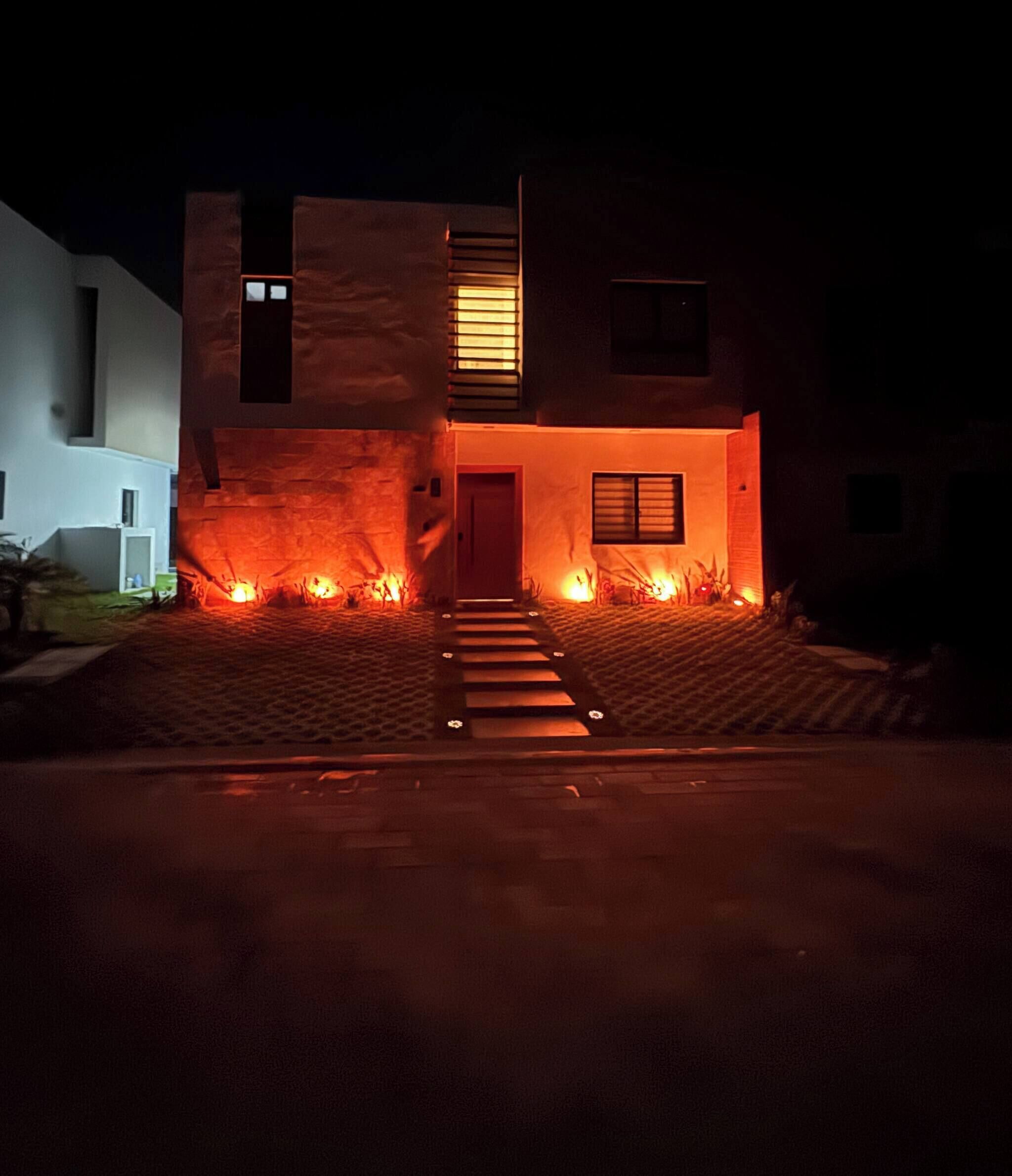 A modern two-story house with a red-lit entrance and a staircase leading to the door.