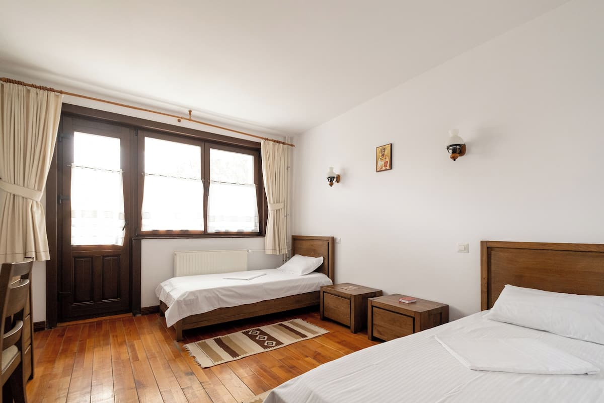 Un dormitorio con dos camas individuales, suelo de madera, ventana con cortinas, radiador y una mesita de noche con un libro.