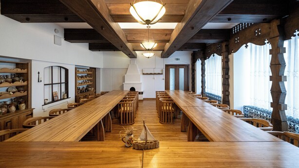 Une longue table en bois, entourée de chaises, un modèle de bateau et des étagères remplies de poteries.