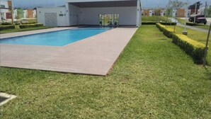 A modern building with a covered swimming pool, surrounded by well-maintained grass and a clear view of distant mountains. - Cozy 2-bedroom house in adorable Ahuachapan with AC / pool (Ahuachapan)