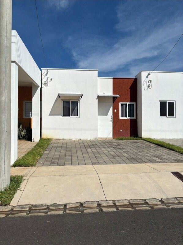 Un edificio residencial moderno con techo plano, entrada pavimentada y pequeño jardín delantero.