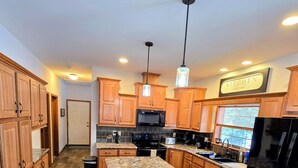 A kitchen with wooden cabinets, a granite countertop island, a black refrigerator, and a microwave. - The Gathering Place, 3 BR sleeps 8, Near Hayward close to lakes and trails. (Hayward)
