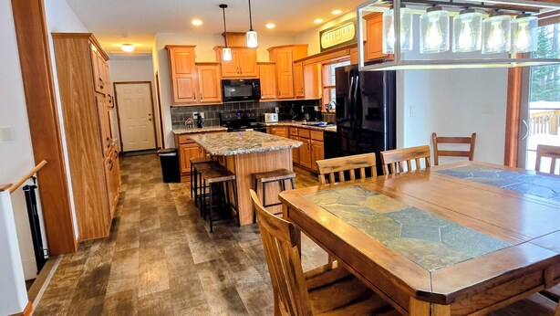 A spacious kitchen with wooden cabinets, a granite countertop, and a dining area with a large table and chairs. - The Gathering Place, 3 BR sleeps 8, Near Hayward close to lakes and trails. (Hayward)