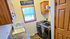 A compact kitchen with wooden cabinets, a granite countertop, a built-in oven, and a laundry sign on the wall. - The Gathering Place, 3 BR sleeps 8, Near Hayward close to lakes and trails. (Hayward)