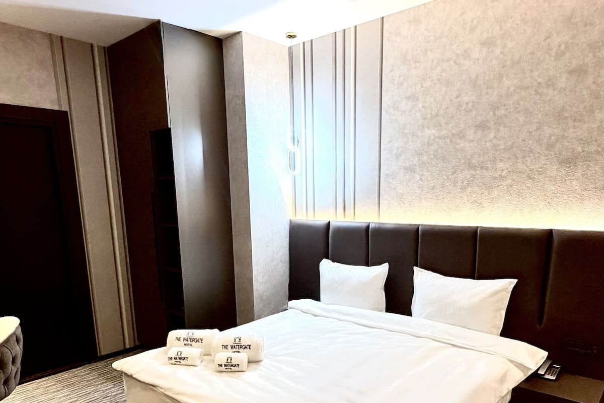 A hotel room with a large bed, a nightstand, a bedside table, and a door.
