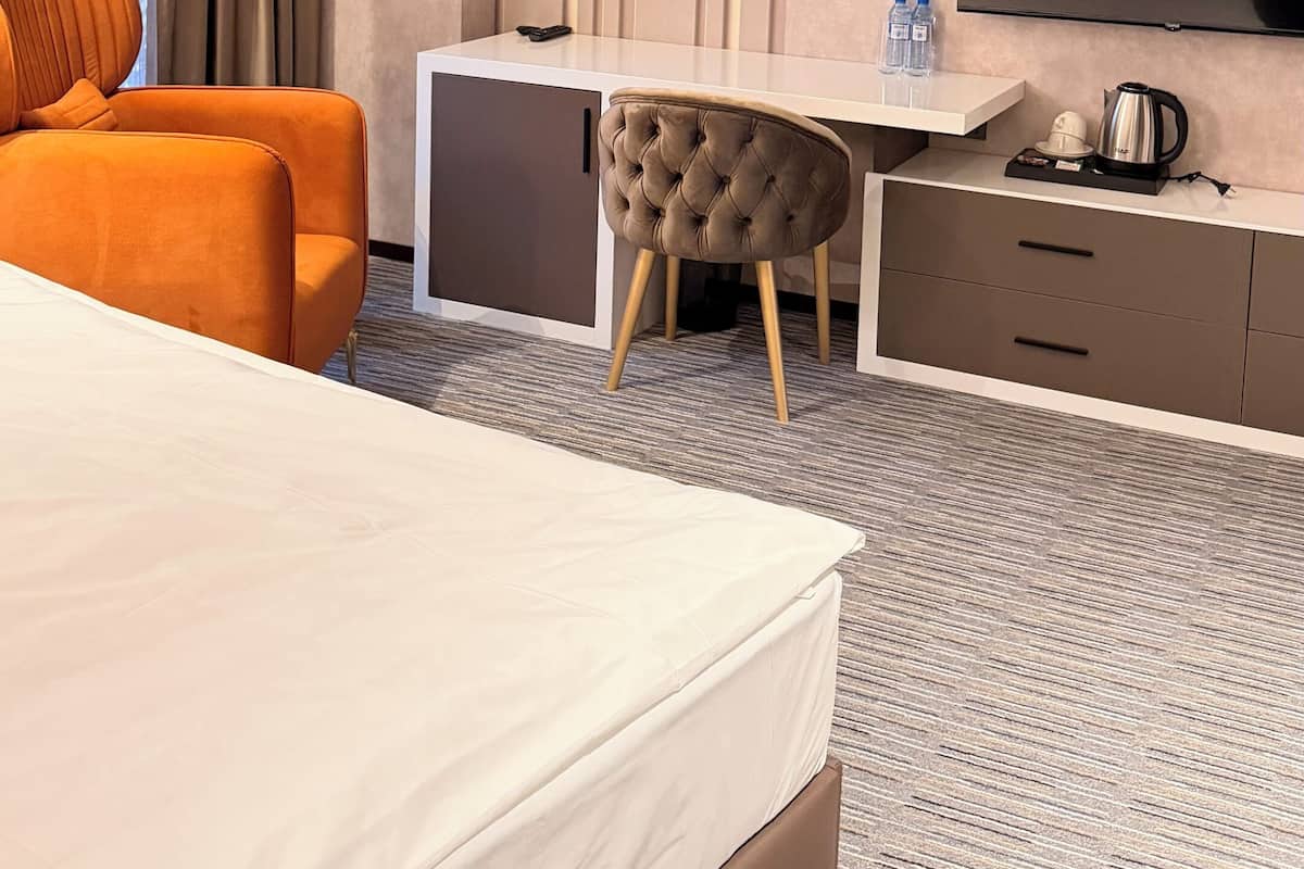 A hotel room with a bed, a desk, a chair, a TV, and a minibar.