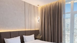 A modern hotel room with a large bed, a nightstand, a wall-mounted light, and a view of the outdoors through a large window. - The Watergate Hotel Baku (Baku)