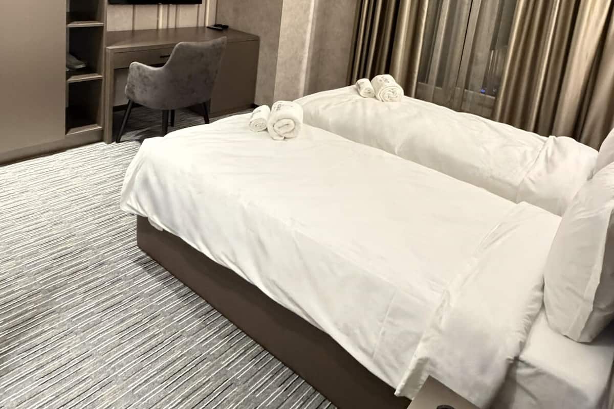 A modern hotel room with a large bed, a desk, a chair, a TV, and a window with curtains.