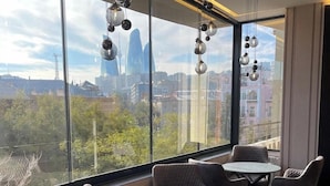 A modern interior with round tables and cushioned chairs, large windows offering a city view, and hanging spherical light fixtures. - The Watergate Hotel Baku (Baku)