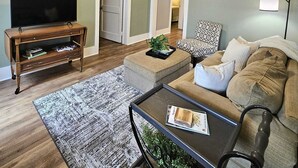 A living room with a television on a wooden stand, a sofa, a coffee table, and a ceiling fan. - Lovely 2-bedroom downtown apartment in charming Lafayette (Lafayette)