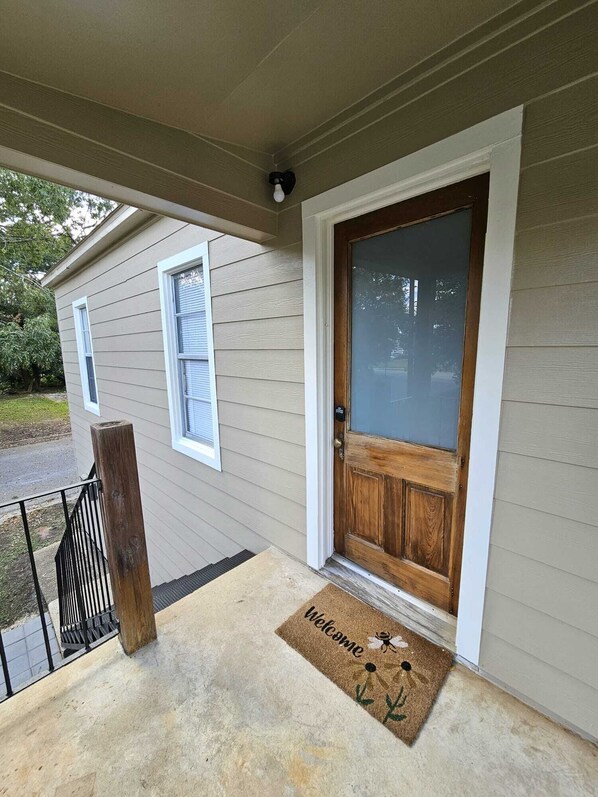 A house with a wooden front door, a welcome mat, and a small porch with a railing.