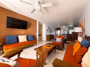 Ein Wohnzimmer mit Backsteinwand, Deckenventilator, Fernseher und Essbereich mit Holztisch und Stühlen.