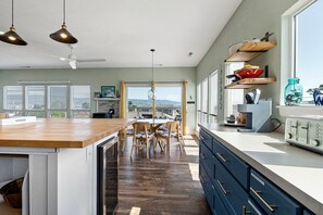 A modern kitchen with a wooden island, dining area, and large windows offering a city view. - This Is It | Ocean Views, Walk to Park & Beach (Crescent City)