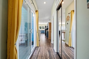 A hallway with sliding glass doors, a wooden floor, and a kitchen area visible through the glass doors. - This Is It | Ocean Views, Walk to Park & Beach (Crescent City)