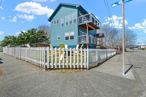 A two-story house with a balcony, a white picket fence, and a street sign. - This Is It | Ocean Views, Walk to Park & Beach (Crescent City)