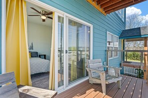 A bedroom with a bed, a ceiling fan, and a sliding glass door leading to a balcony with wooden furniture. - This Is It | Ocean Views, Walk to Park & Beach (Crescent City)
