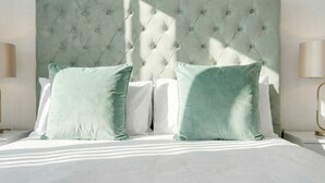 Uma cama com cabeceira estofada, duas almofadas e abajures laterais.