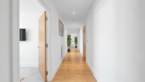 Corredor com piso de madeira, paredes brancas e um vaso de planta.