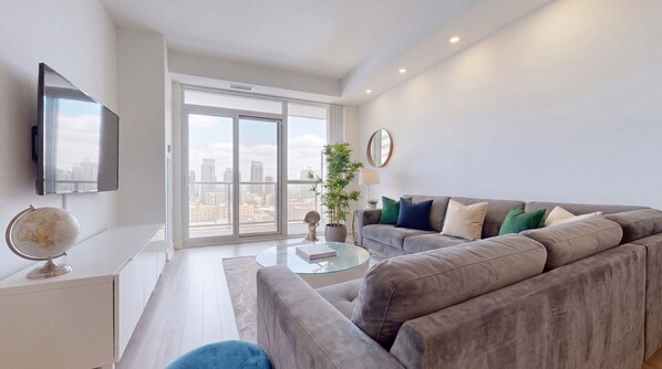 A modern living room with a grey sofa, a glass coffee table, a globe, and a large window with a city view. - Luxury 2-Bed London Apartment Greenwich & Canary Wharf (London)