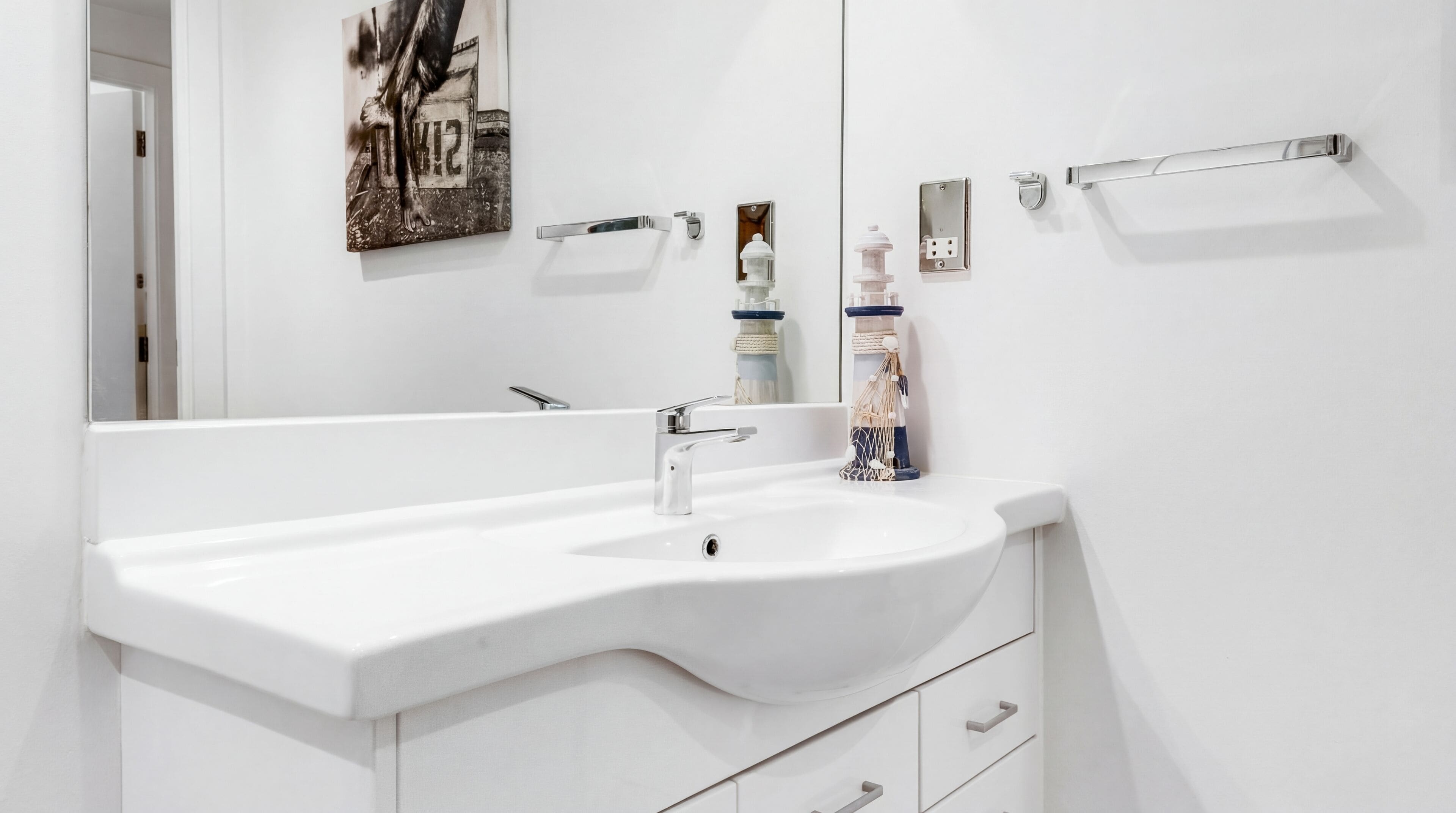 Un bagno bianco con un lavandino ampio, uno specchio e un portaservizi.