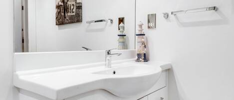 A white bathroom with a large sink, a mirror, and a towel rack.