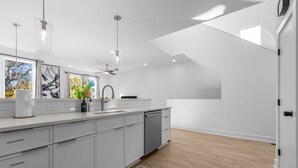 Una cocina moderna con armarios blancos, lavavajillas y un amplio ventanal.