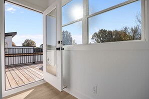 Offene Tür, die auf einen Balkon mit Holzboden und Blick auf Bäume und ein Gebäude führt.