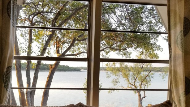 A window with a view of a calm lake and trees. - Lakeside Cabin #4 (Eastland County)