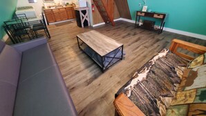 A living room with a wooden floor, a sofa, a coffee table, a patterned rug, a TV, a fireplace, and a kitchen in the background. - Lakeside Cabin #4 (Eastland County)