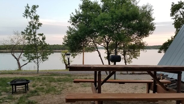 Ett picknickbord med en grill och bänkar, omgivet av träd och med utsikt över en sjö.