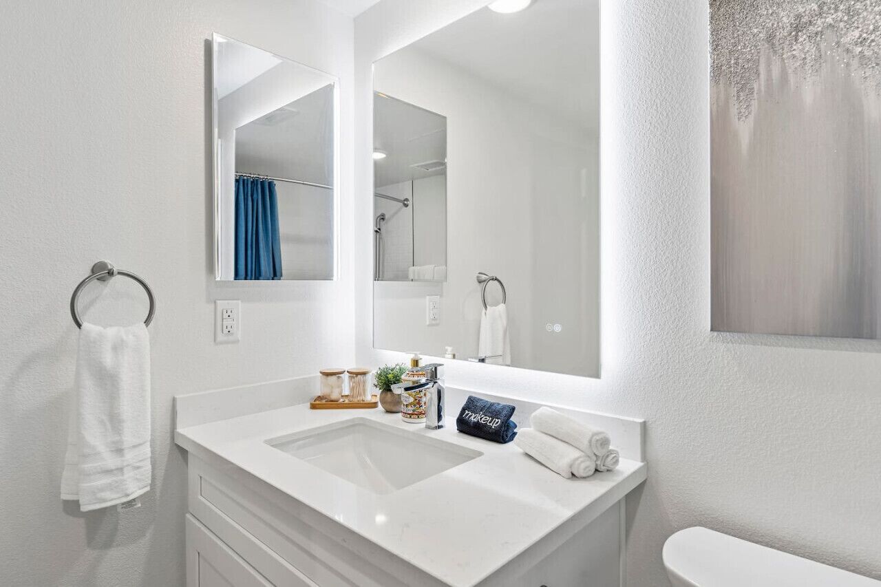 Ein modernes Badezimmer mit einem weißen Waschbecken, zwei Spiegeln, einem Handtuchhalter und einer Toilette.