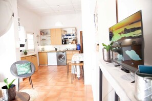 A modern kitchen with a washing machine, a dining area with a chair, and a TV mounted on the wall. - Central 2-bedroom house in Bohemian Obs (Cape Town)