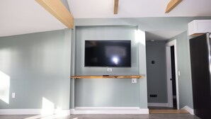 A room with a mounted TV, wooden beams on the ceiling, and a door leading to another room. - Modern Hermon Pond Retreat: 25ft to Shore, 15m to Bangor, Fishing & Kayak Launch (Hermon)