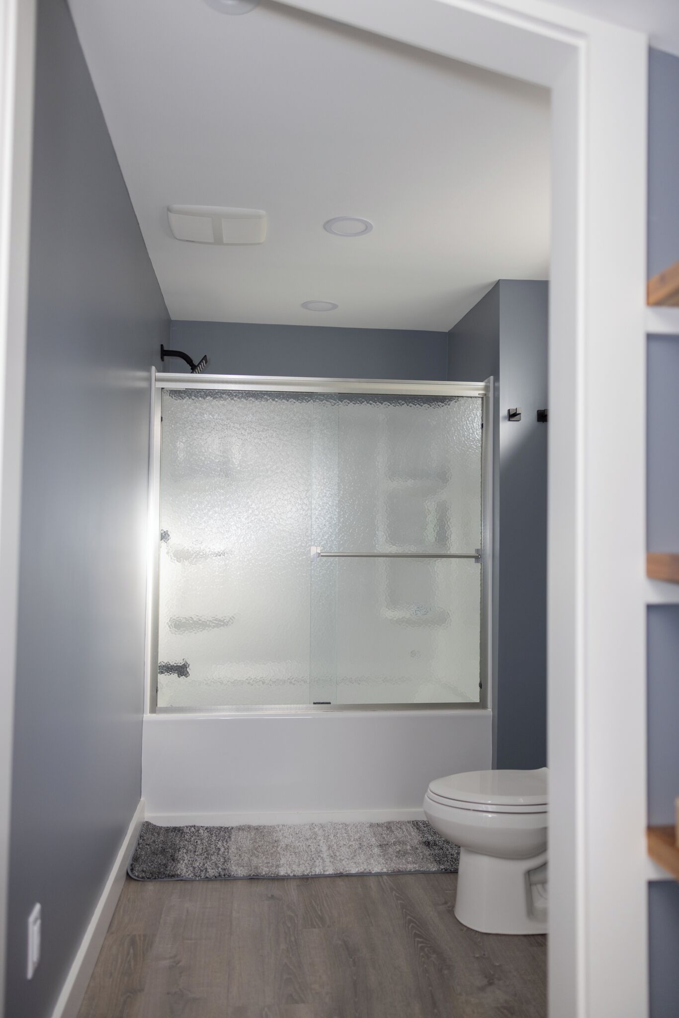 A modern bathroom with a glass-enclosed shower, a toilet, and a wooden floor.