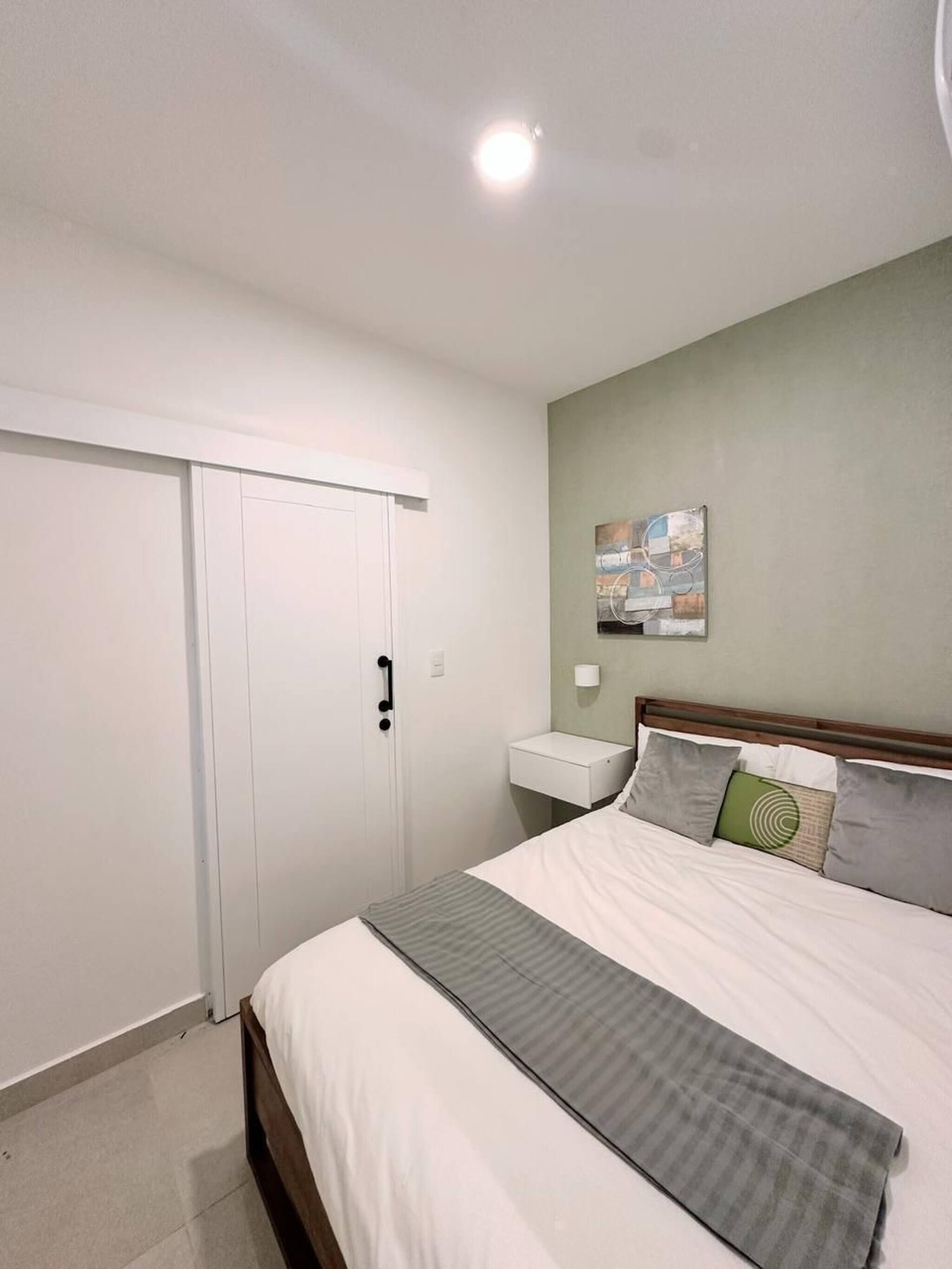 A bedroom with a bed, a nightstand, a wall-mounted lamp, and a door.