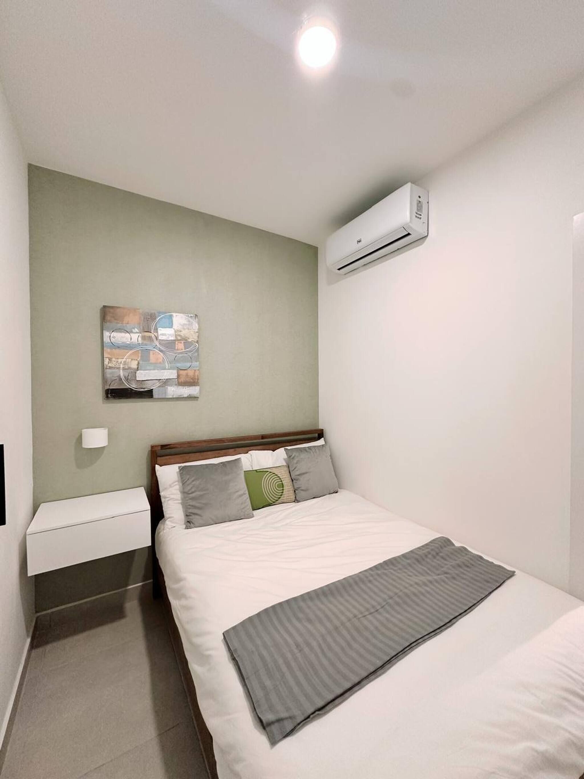 A neatly arranged bedroom with a bed, bedside table, and an air conditioning unit on the wall.
