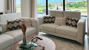 A modern living room with two sofas, a coffee table, and a view of a cityscape through large windows. - Azzure Cap Cana Get Away (Punta Cana)