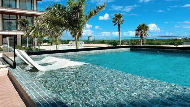 A swimming pool with clear blue water, surrounded by palm trees and a modern building with large windows. - Azzure Cap Cana Get Away (Punta Cana)
