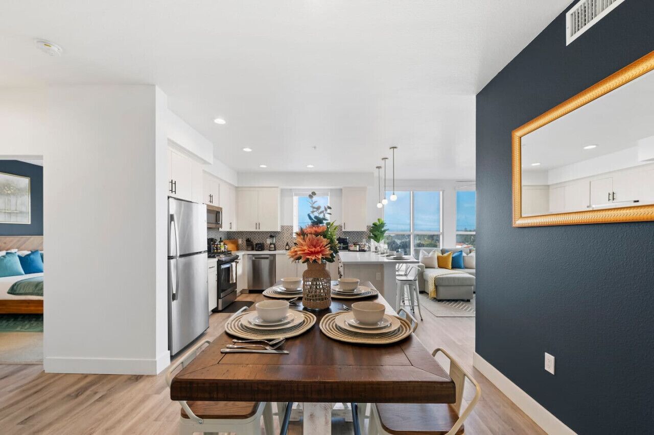 A modern kitchen with a dining area, white cabinets, and a large window.