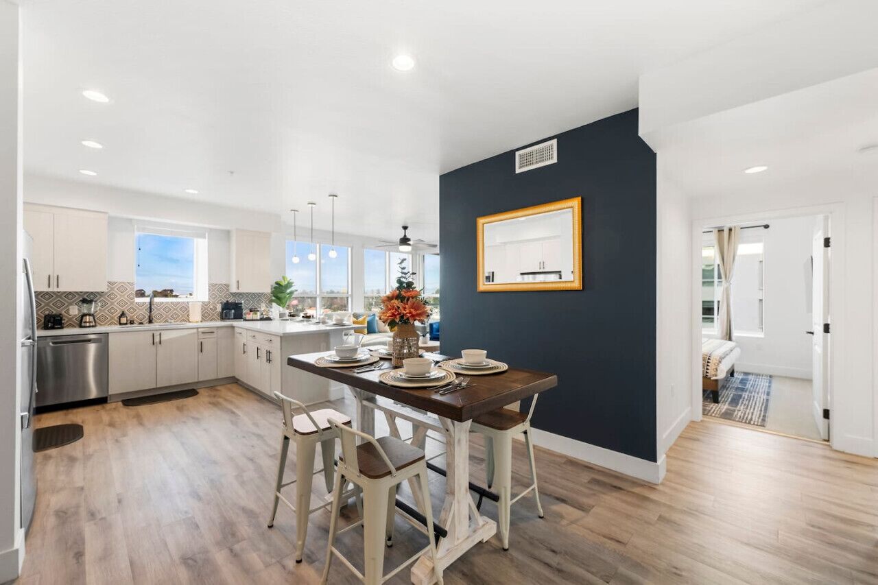 A modern kitchen with white cabinets, a dark accent wall, and a dining area with bar stools.