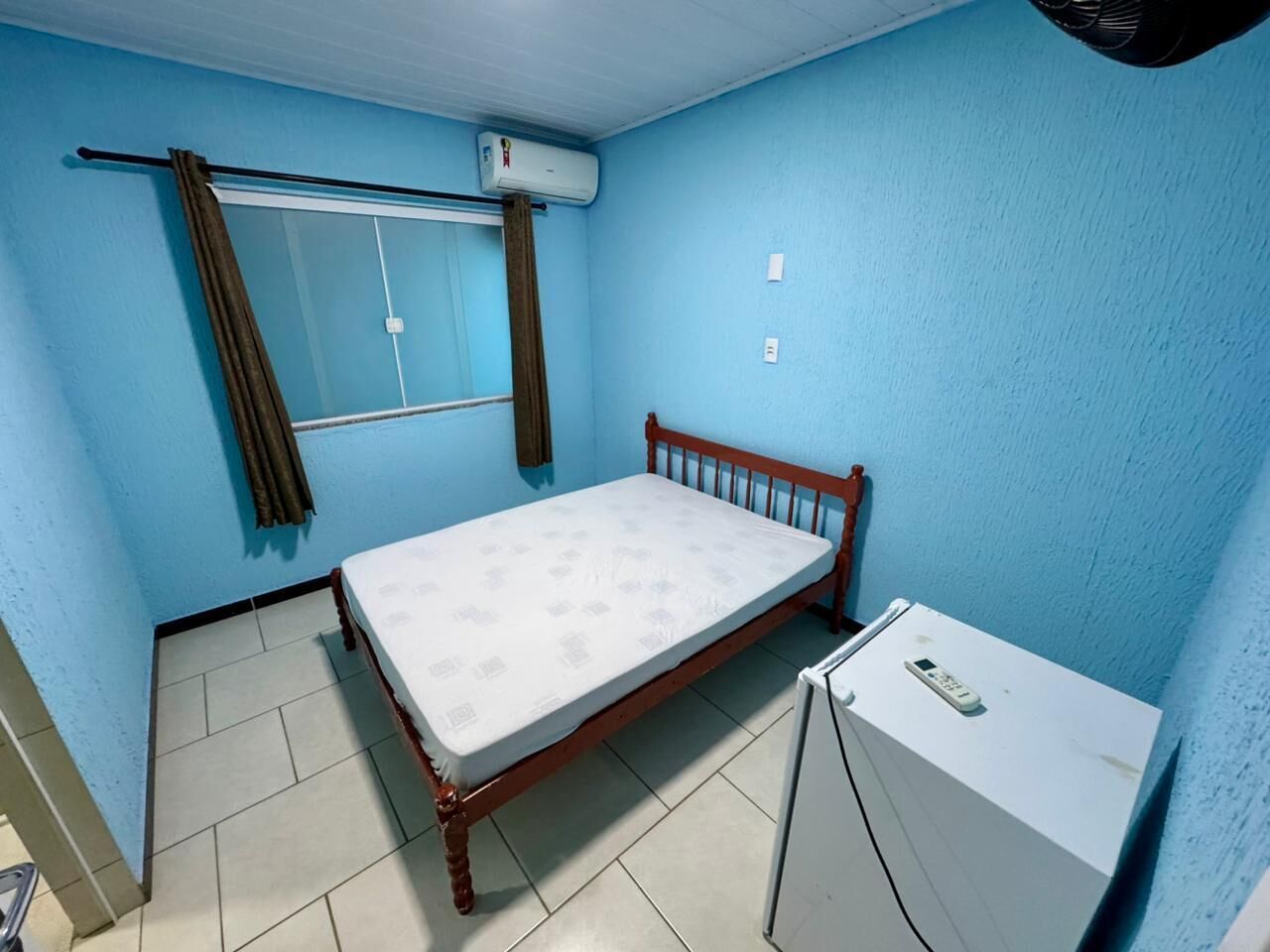 Un petit appartement d’une seule pièce, comprenant un lit, un petit bureau et un appareil de climatisation.