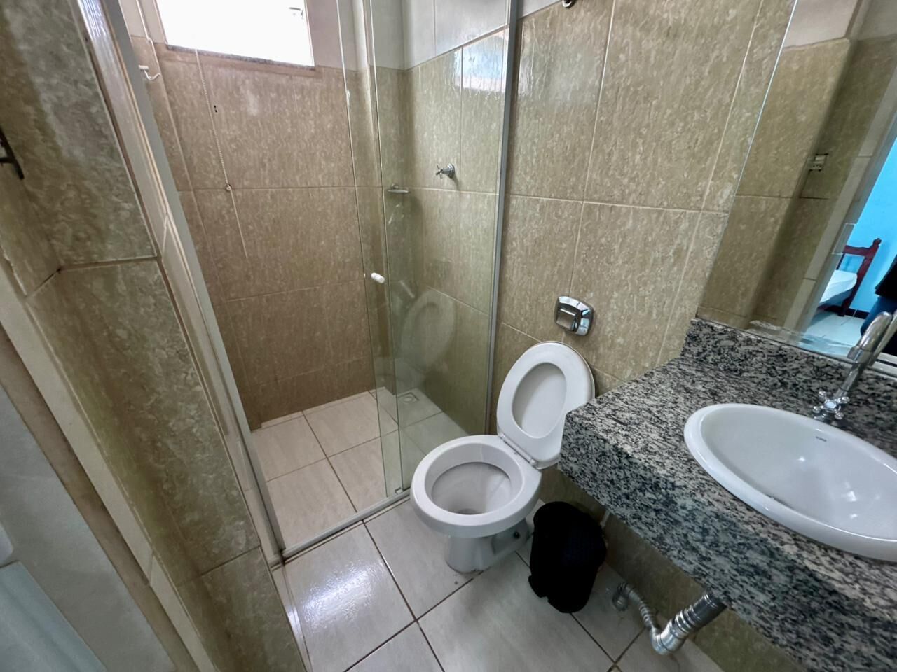 Et badeværelse med en brusekabine i glas, toilet og en vask med bordplade i granit.