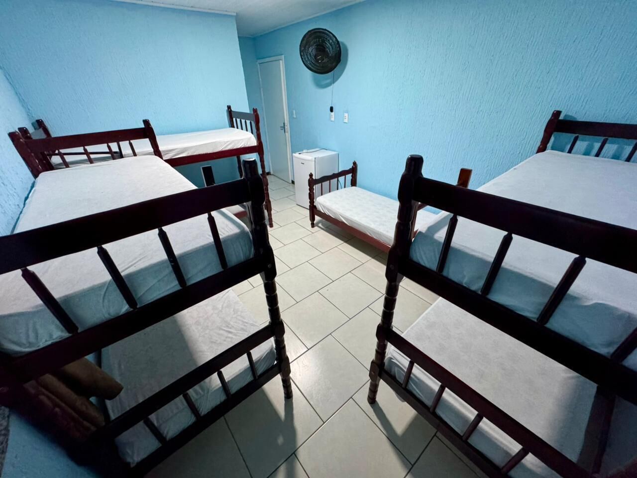 Une chambre de dortoir avec quatre lits superposés, une petite table, un ventilateur et une porte.
