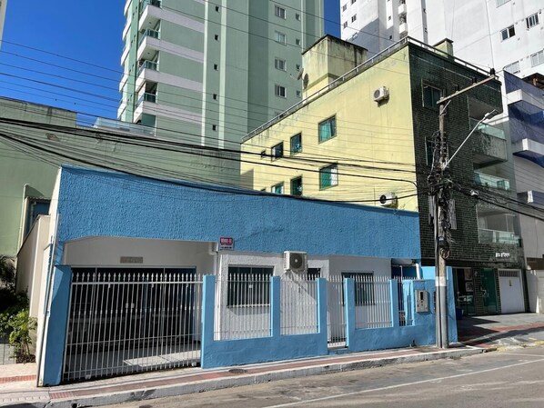 Un edificio con fachada azul, entrada protegida por una verja y unidad de aire acondicionado visible.