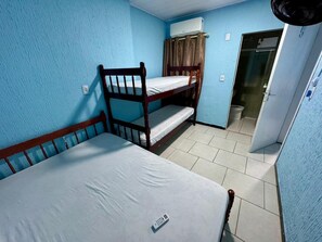 Una habitación de hotel pequeña y sencilla con una cama individual superpuesta, un escritorio, una silla, una ventana con cortinas y una puerta que da a un baño.