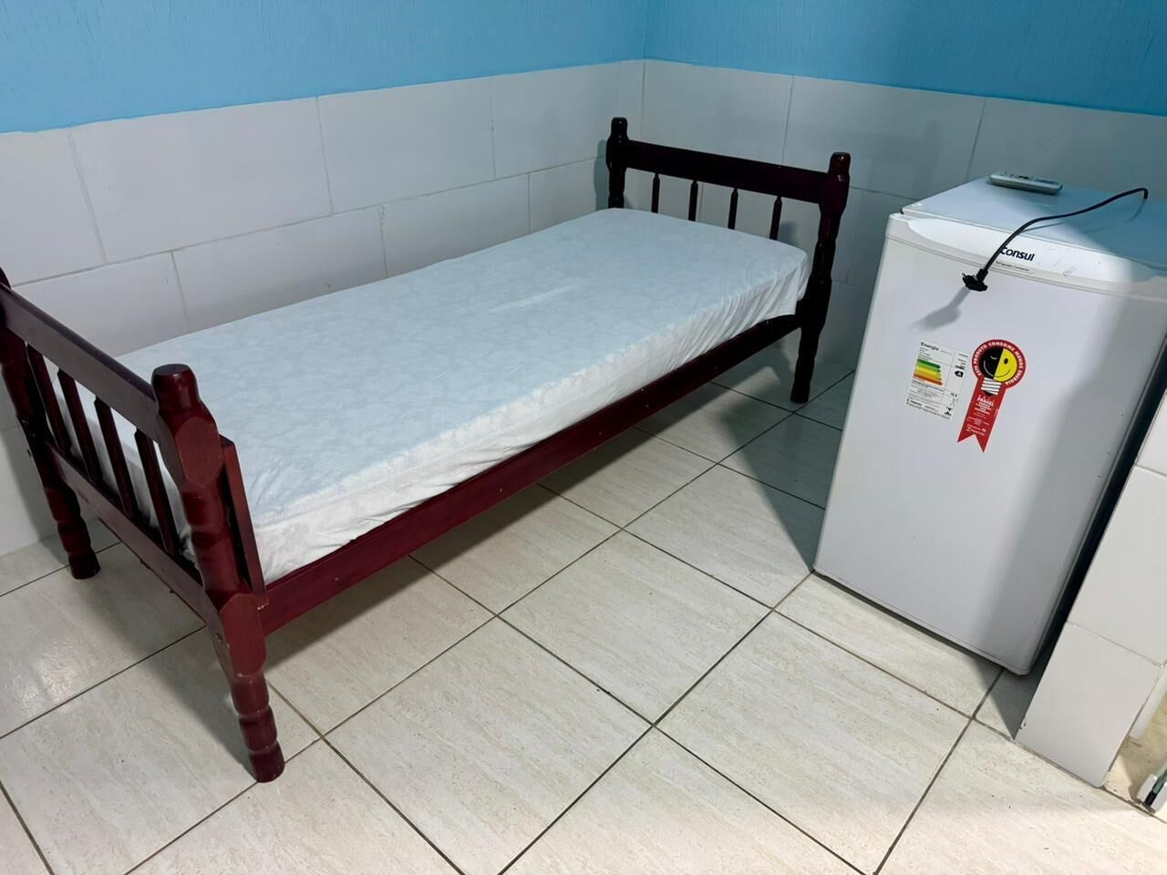 A small room with a wooden bed and a white refrigerator.