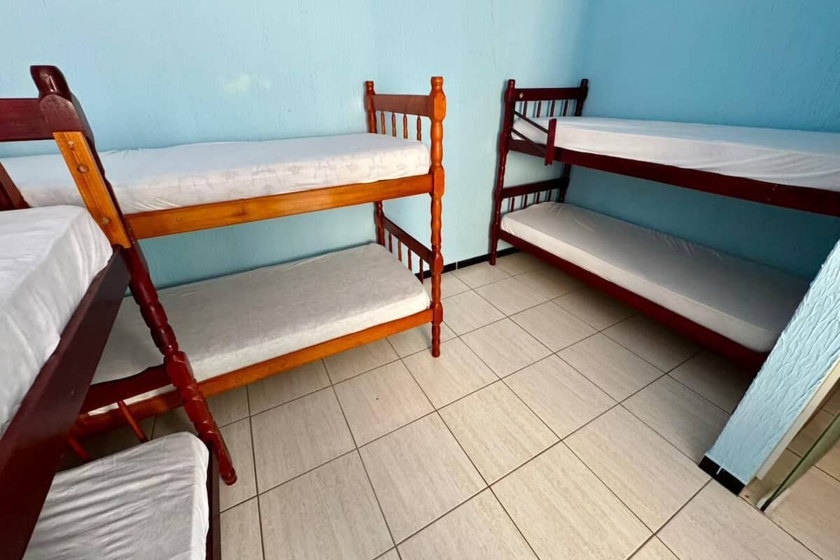 Una habitación con tres literas de madera, paredes azul claro, suelo de baldosas y una ventana a la derecha.