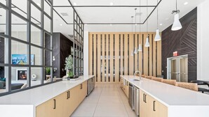 Een moderne keuken met een centraal kookeiland, hanglampen en een uitzicht door een glazen wand op een woonkamer met een open haard.