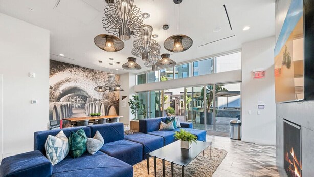Een moderne lobby met een blauwe modulaire bank, een open haard en een groot raam met uitzicht op de stad.