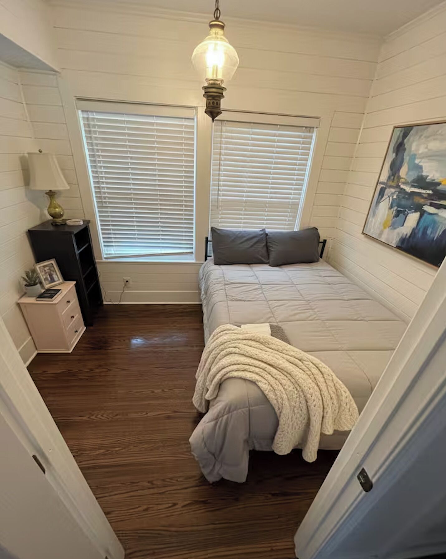 Quarto com cama, mesa de cabeceira, luminária e um quadro na parede.